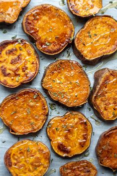 baked sweet potatoes on a baking sheet ready to be cooked in the oven with herbs sprinkled on top