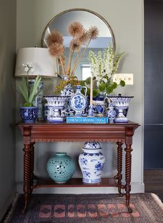 blue and white vases on a table with a mirror in the corner behind them