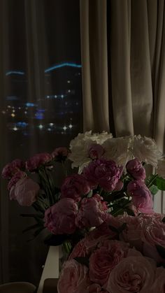 a vase filled with pink and white flowers on top of a table next to a window