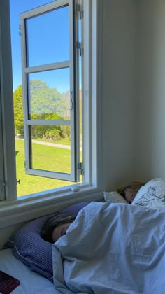 an unmade bed in front of a window with the view of a field outside