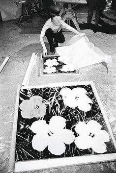 a man kneeling down on the ground next to two paintings with flowers painted on them