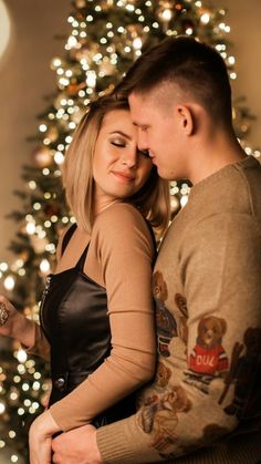 a man and woman standing in front of a christmas tree with their arms around each other