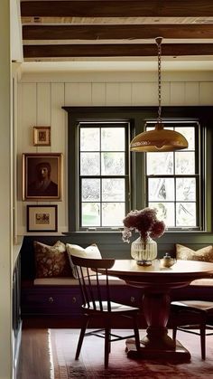 a dining room table with four chairs and a bench in front of two windows that have framed pictures on the wall