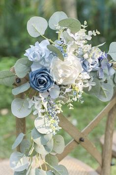 a blue and white bouquet sitting on top of a wooden chair with greenery around it