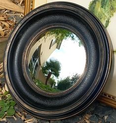 a round mirror sitting on the ground next to a wall with a painting behind it