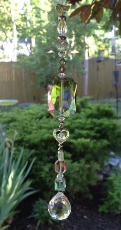 a glass wind chime hanging from a tree in the yard with lots of greenery behind it