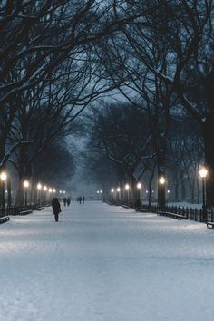 a person walking down a snow covered sidewalk at night with street lights in the distance