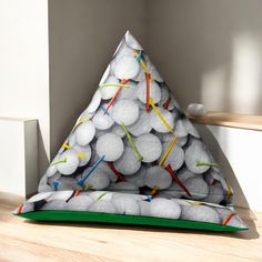 a triangle shaped pillow with golf balls on it sitting on a wooden floor in front of a white wall