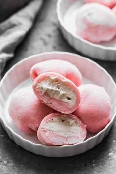 three white bowls filled with pink donuts on top of a gray countertop next to a towel