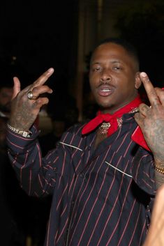 a man in a striped shirt making the peace sign with his hands and wearing a red scarf around his neck