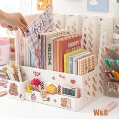 a person is holding a book in a white holder on a desk with other books and stationery items