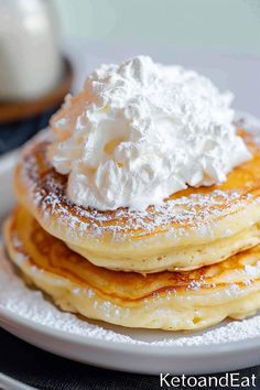 a stack of pancakes topped with whipped cream and powdered sugar on a white plate