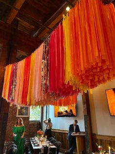 people are sitting at tables in a restaurant with colorful streamers hanging from the ceiling