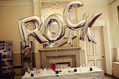 a table topped with lots of silver foil balloons next to a fire place filled with wine glasses