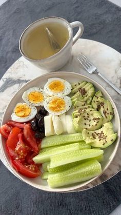 a white plate topped with cucumbers, tomatoes and hard boiled eggs next to a cup of tea