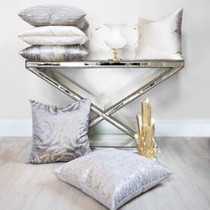 pillows and decorative items sit on a mirrored table in front of a white wall with gold accents