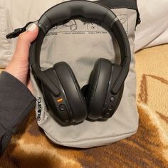 a pair of black headphones sitting on top of a gray bag next to a pillow