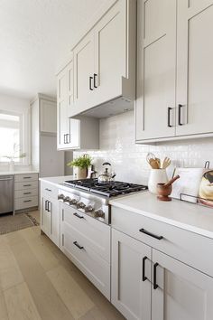 a kitchen with white cabinets and an oven in the center is seen from across the room