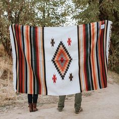 a person standing on a dirt road holding up a blanket with an orange and black design