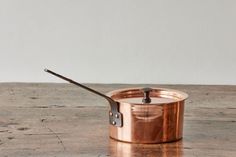 a copper colored pot with a wooden handle on a wood table next to a white wall