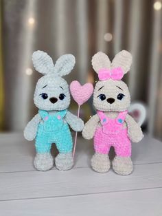 two crocheted stuffed animals holding a heart shaped lollipop in their hands