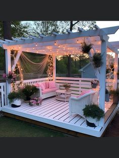 an outdoor deck with white furniture and string lights on the ceiling, surrounded by potted plants