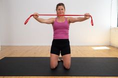 a woman sitting on a yoga mat holding a red bar over her head with both hands