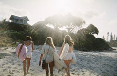 three girls walking on the beach with their surfboards