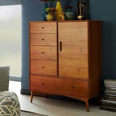 a tall wooden cabinet sitting in a living room next to a chair and table with vases on top of it