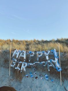 a happy birthday message made out of plastic bottles on the beach with blue balloons and streamers