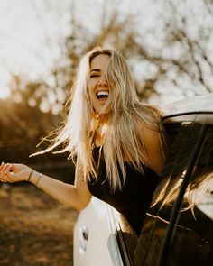 a woman is laughing and leaning out the window of a car