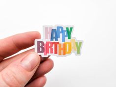 a hand holding a sticker with the words happy birthday written in rainbow colors on it