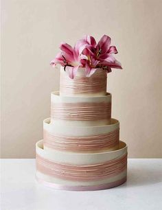 a three tiered cake with pink flowers in the middle on a white countertop