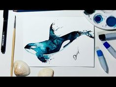 a drawing of an orca whale on paper next to paintbrushes and other art supplies