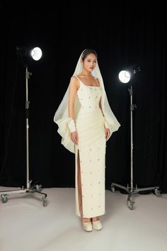 a woman in a white dress and veil posing for the camera with lights behind her