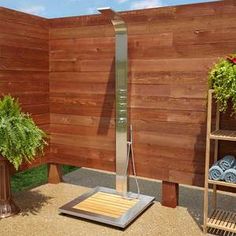 an outdoor shower in the middle of a wooden wall with plants and towels on it