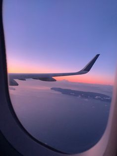 the wing of an airplane as it flies over water and land at sunset or dawn