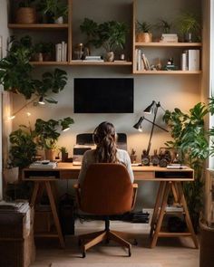 a woman sitting at a desk in front of a computer monitor with plants on it