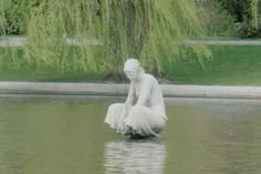 a statue sitting on top of a body of water next to a lush green tree