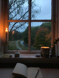 an open book sitting on top of a window sill next to a lit candle