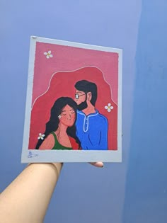 a hand holding up a painting of a man and woman in front of a blue sky