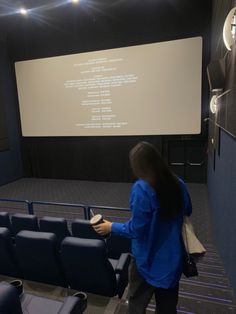 a woman standing in front of a projection screen holding a book and looking at it