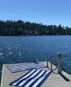 two towels are laying on the end of a dock next to some water and trees