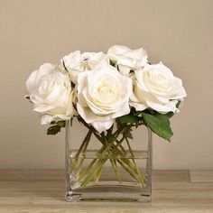 white roses in a clear vase on a wooden table