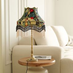 a table with a lamp on top of it in front of a couch and white walls