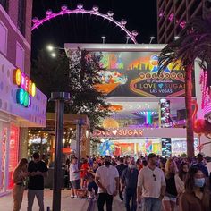 a crowd of people walking down a street next to tall buildings with neon lights on them