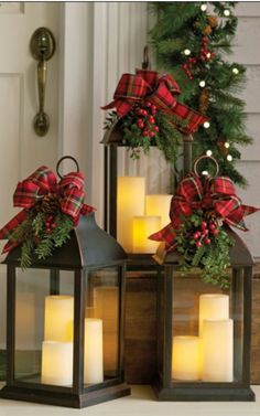 two lanterns with christmas decorations on them sitting in front of a door, one is lit and the other has candles