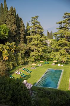 an outdoor swimming pool surrounded by trees and lawn chairs with umbrellas on the grass