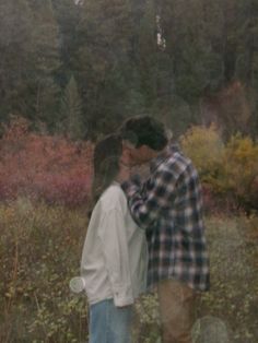 a man and woman kissing in front of some trees with fall foliages behind them