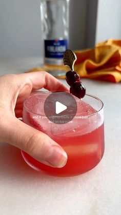 a hand holding a glass with a cherry on top and a garnish in it